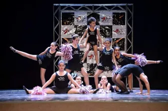 Alunas da oficina de dança se apresentando no palco, com pompons